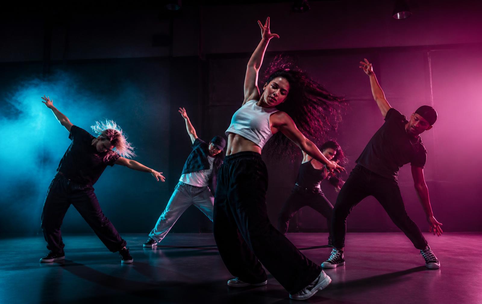 Dancers rehearsing together under neon studio lighting